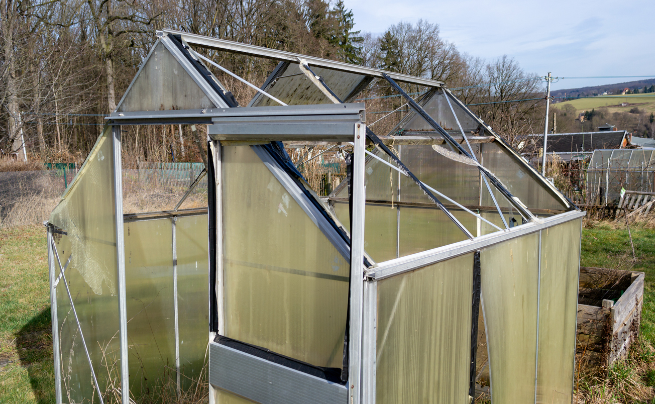 A glass greenhouse with smashed panels from a storm